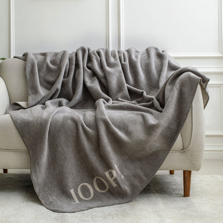 Spread Home Joop blanket in plush wool, sand natural color, draped over a beige sofa for added comfort and style.