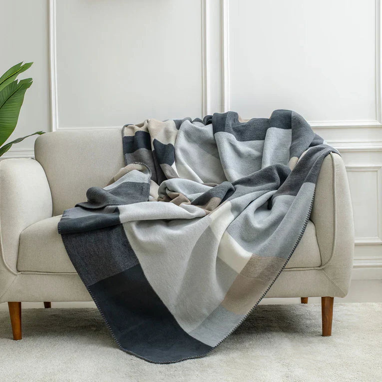 Spread Home cozy blanket in neutral tones, draped over a beige sofa, adding warmth and style to any living space with a soft, geometric pattern.